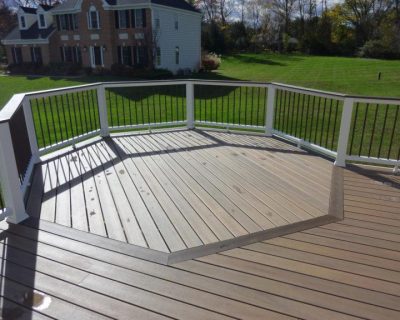 a wooden deck with white railings and a house in the background
